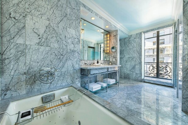 Une salle de bain luxueuse avec des murs en marbre, une grande baignoire, un meuble-lavabo avec un miroir et une vue sur l’extérieur.