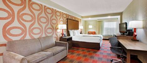 A hotel room with a sofa, a bed, a desk, and a television.