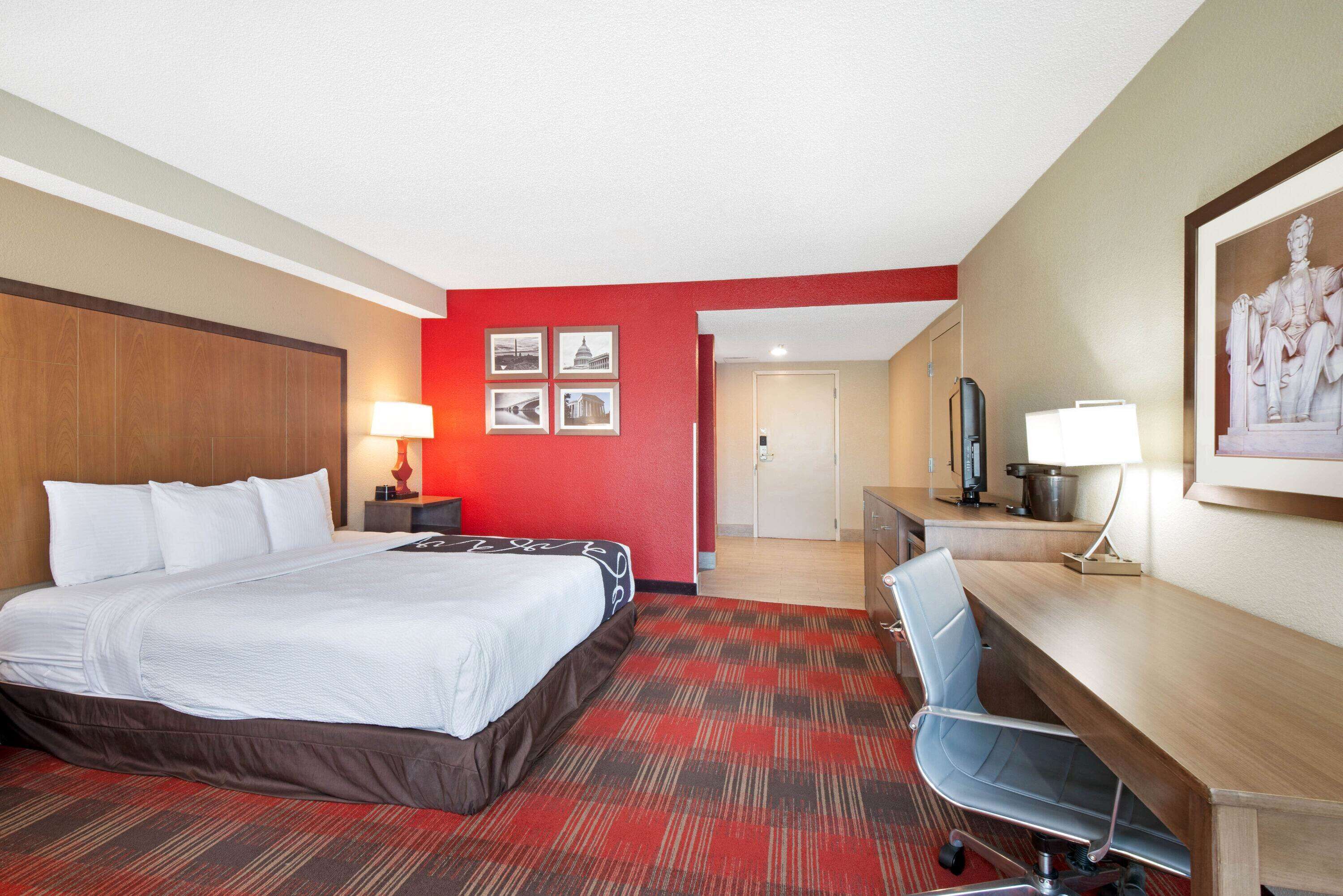 Une chambre d’hôtel avec un lit, un bureau, une chaise et une moquette rouge.
