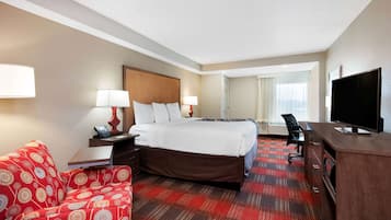 A hotel room with a bed, a desk, a television, and a red patterned sofa.