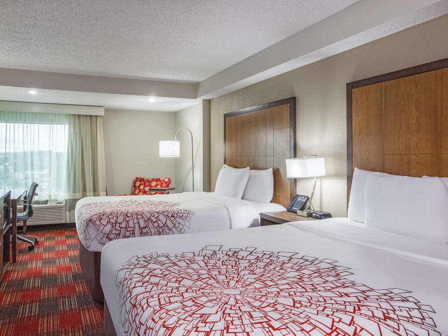 Habitación de hotel con dos camas, un escritorio, un televisor y una ventana con cortinas.