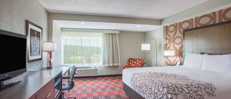 A hotel room with a bed, a TV, a desk, and a window with curtains.