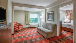 Habitación de hotel con sofá, televisión, ventana con cortinas, lámpara y cama.