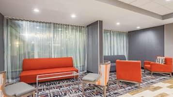 A modern hotel room with a red sofa, two striped armchairs, a glass coffee table, and a patterned carpet.