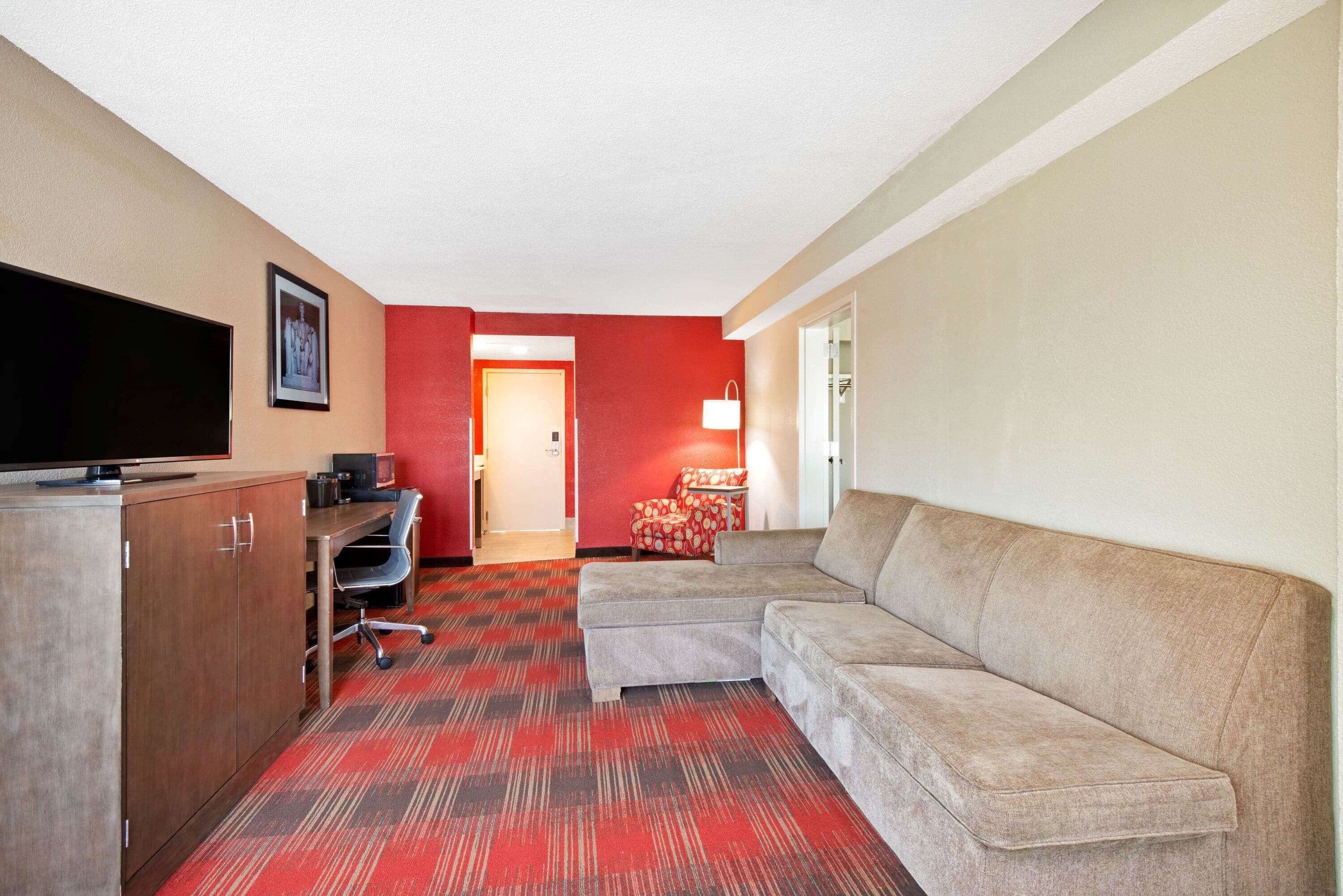 A hotel room with a sofa, TV, desk, and a red carpeted floor.