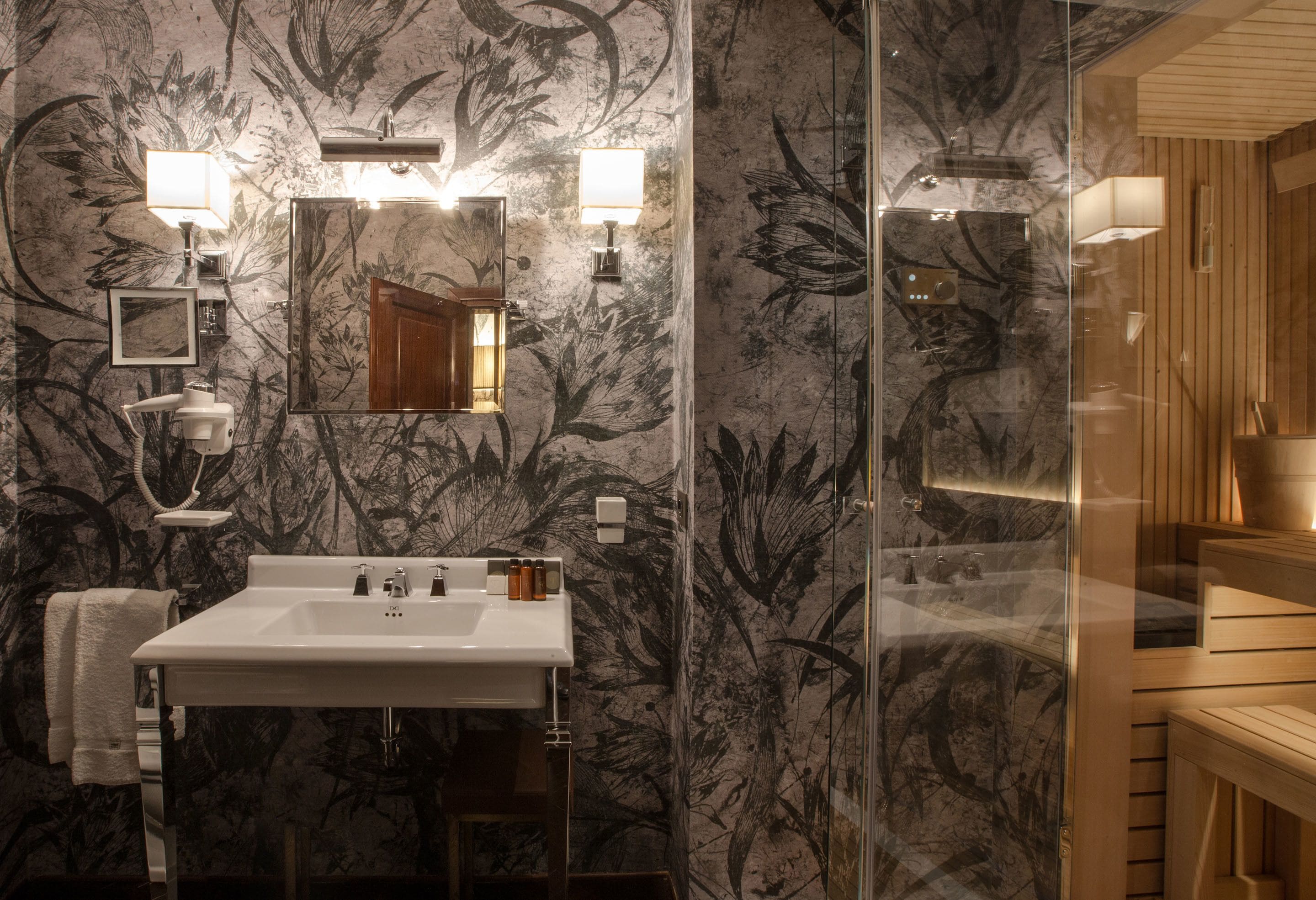 A bathroom with a marble wall, a sink with a mirror, and a shower area.