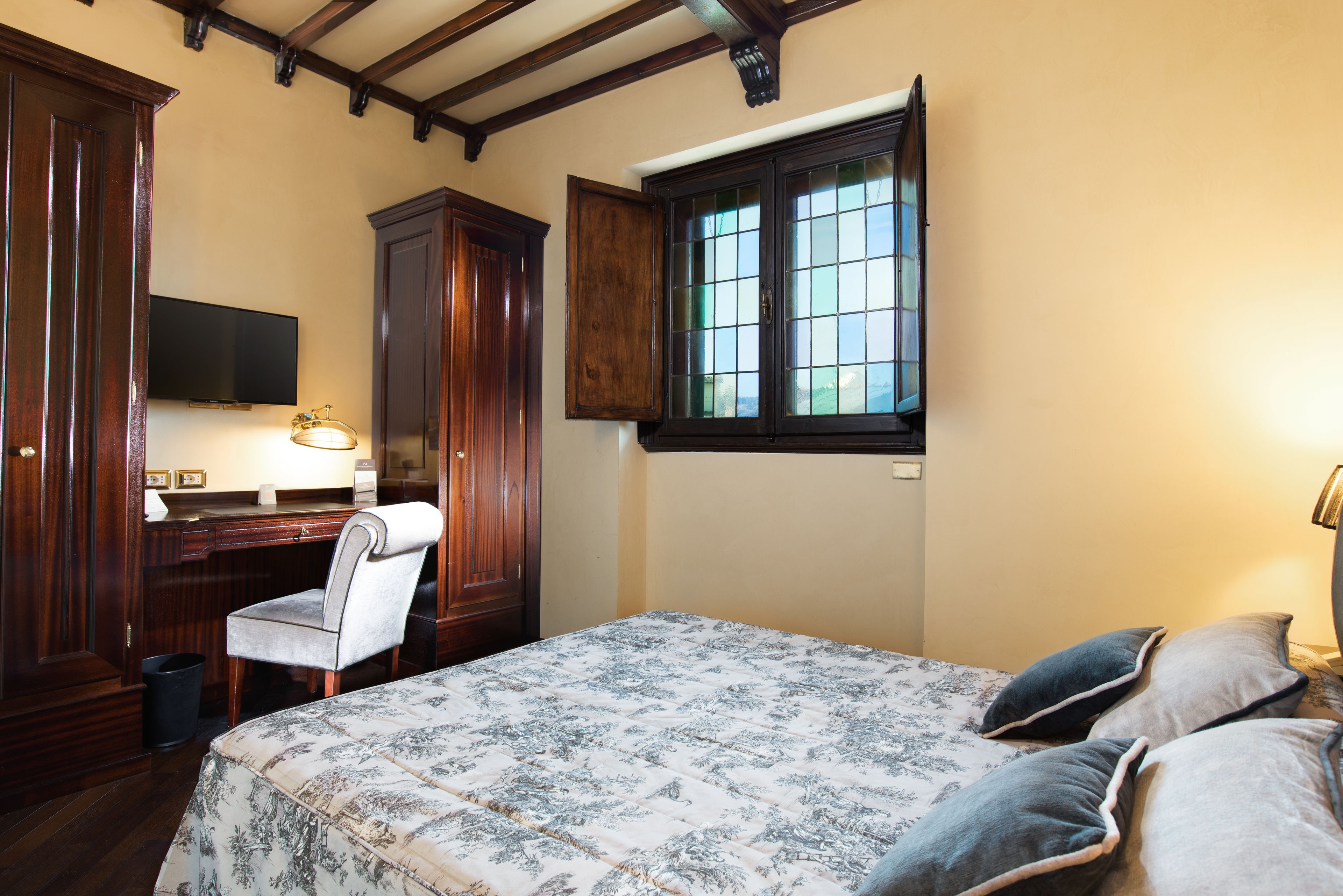 Un dormitorio con cama, escritorio, silla, televisor y ventana.