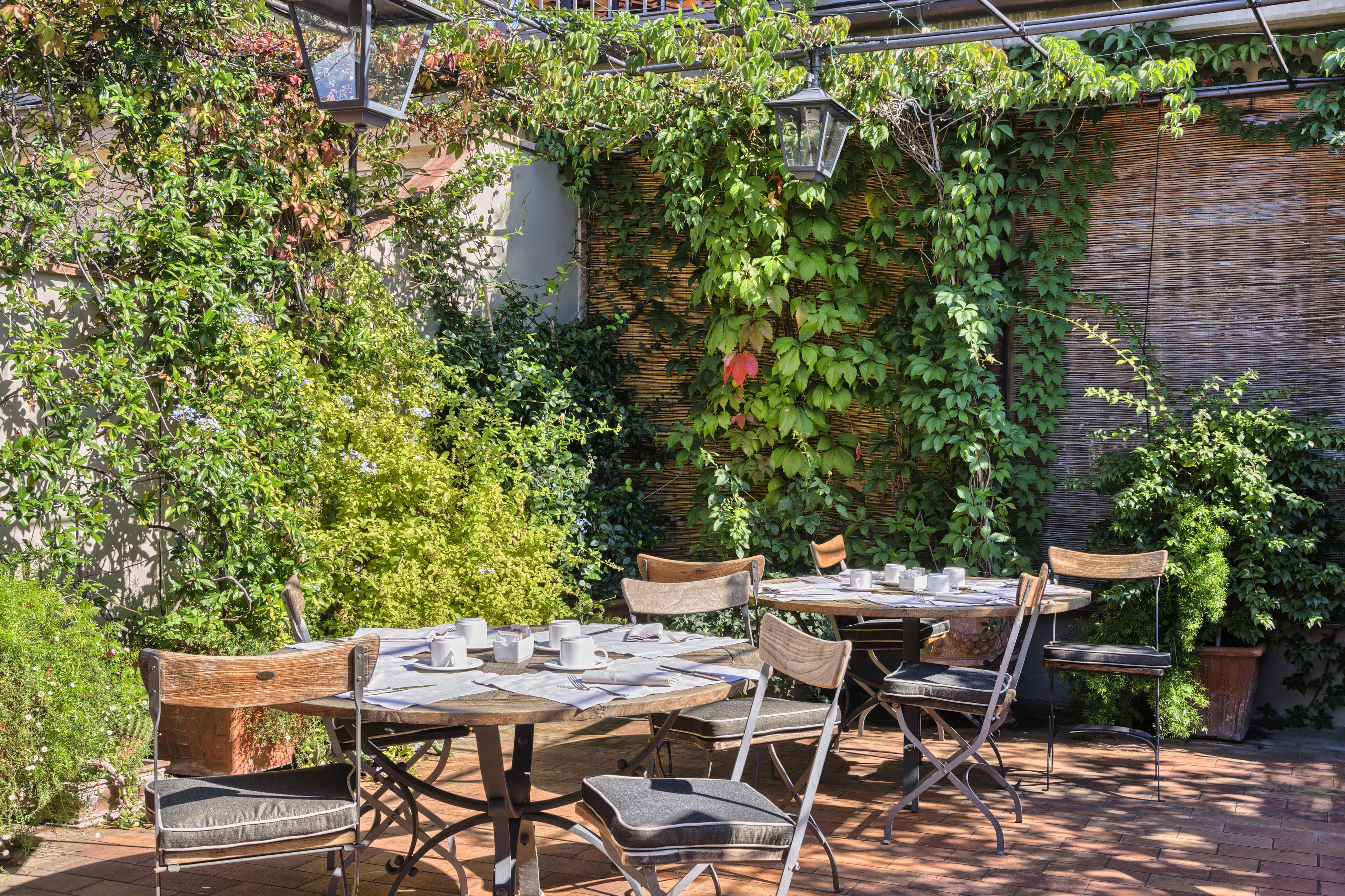 An outdoor patio with tables and chairs, surrounded by lush greenery and a bamboo wall.