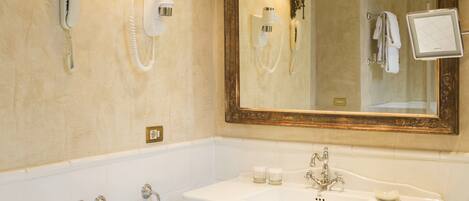 A bathroom with a large mirror, a bathtub, a sink, and two wall-mounted lamps.