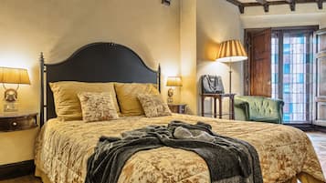 A well-appointed bedroom with a large bed, two bedside tables with lamps, a green armchair, and a window with a view.
