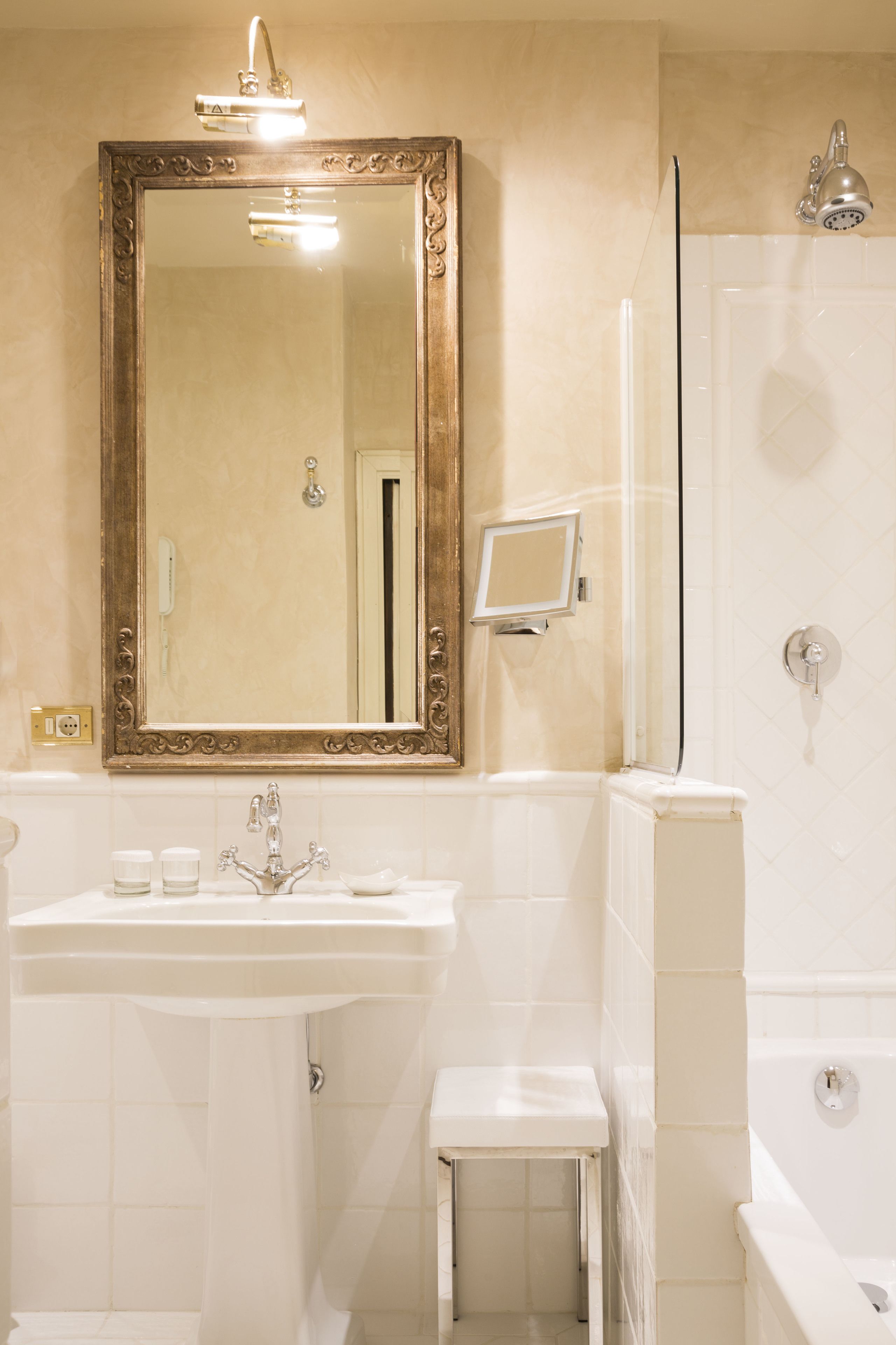 Un bagno con uno specchio grande, un lavandino, uno sgabello piccolo, una doccia e un water.