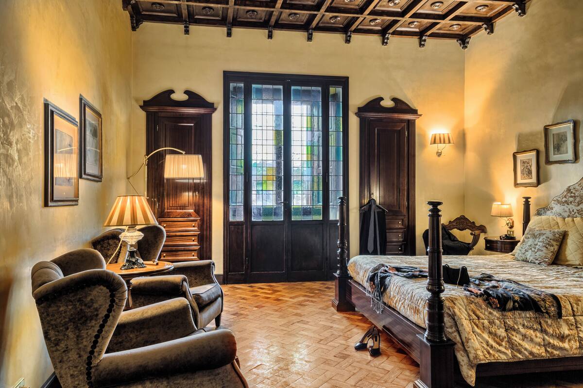 Ein Schlafzimmer mit einem großen Bett, Holzboden, einer Tür mit Glasfeldern und einer Decke mit freiliegenden Balken.