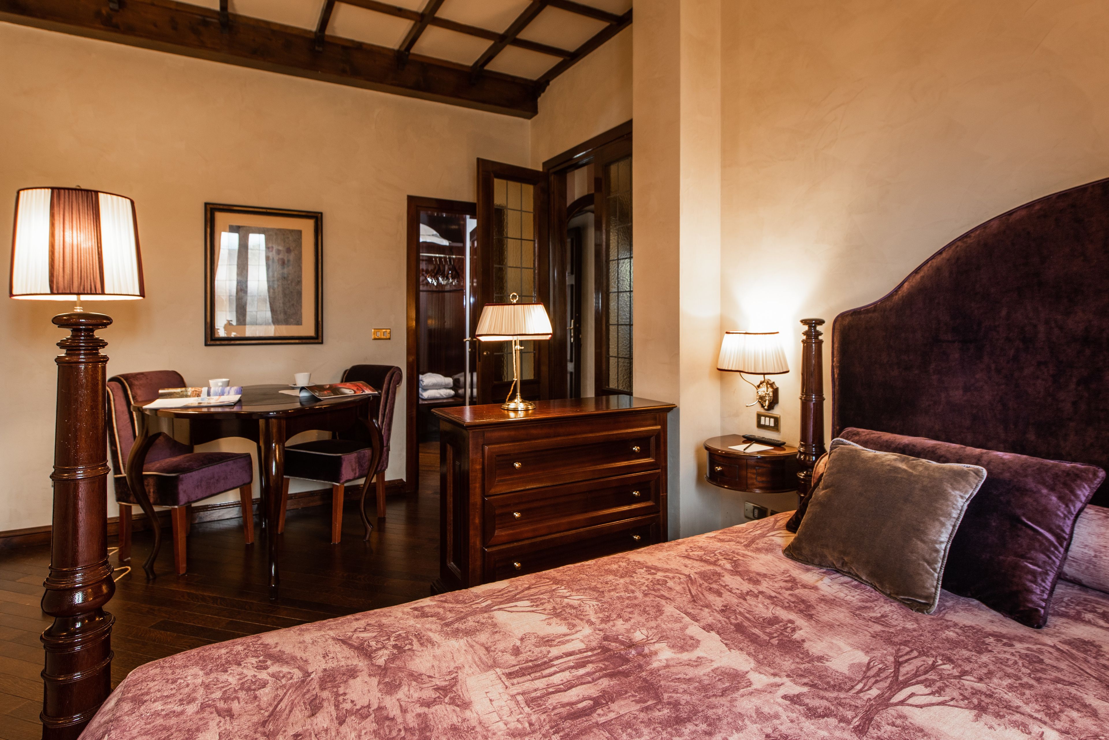 A hotel room with a large bed, a wooden dresser, a desk with chairs, and a dining table.