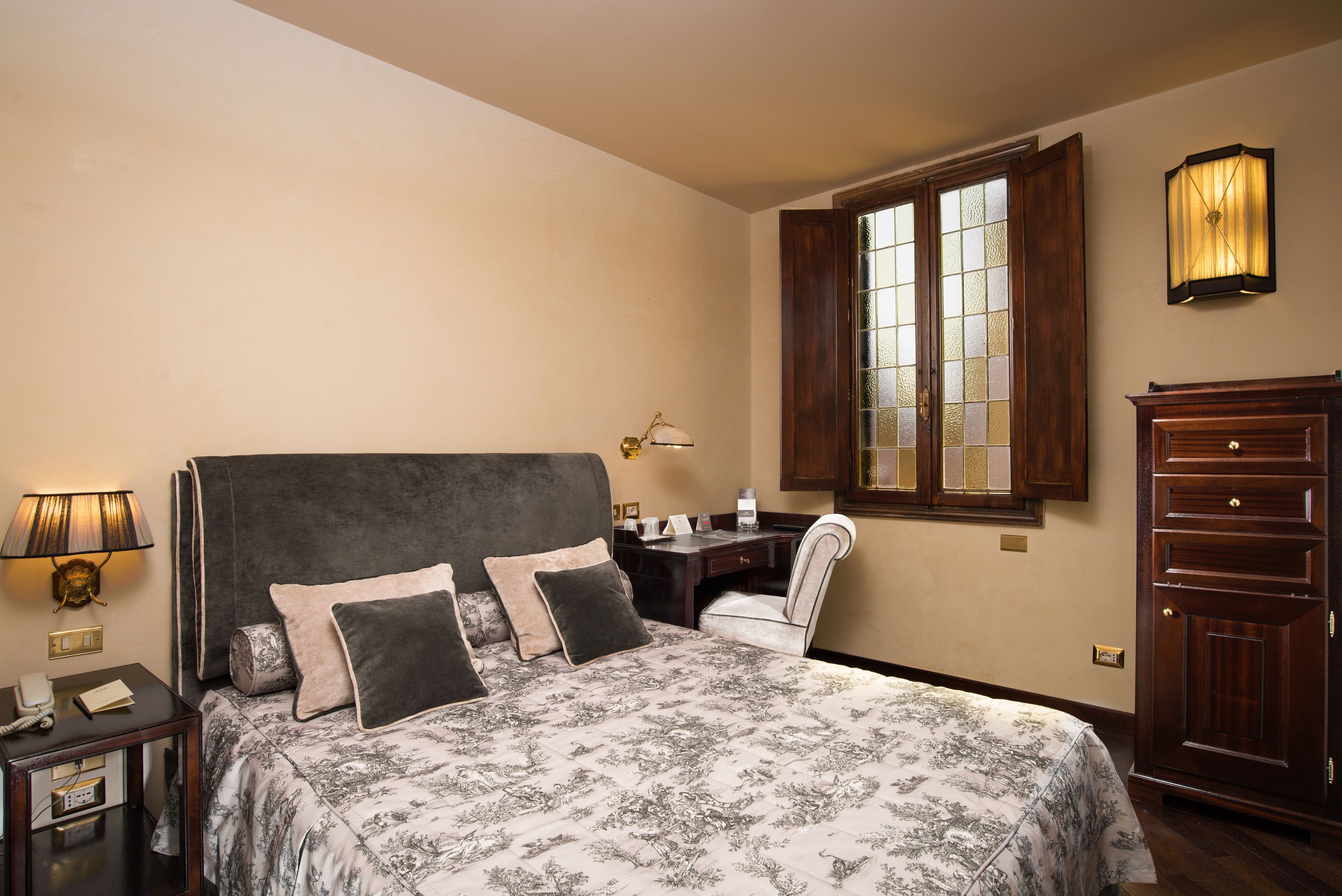 Habitación de hotel con una cama grande, un escritorio, una silla, una lámpara y un armario.