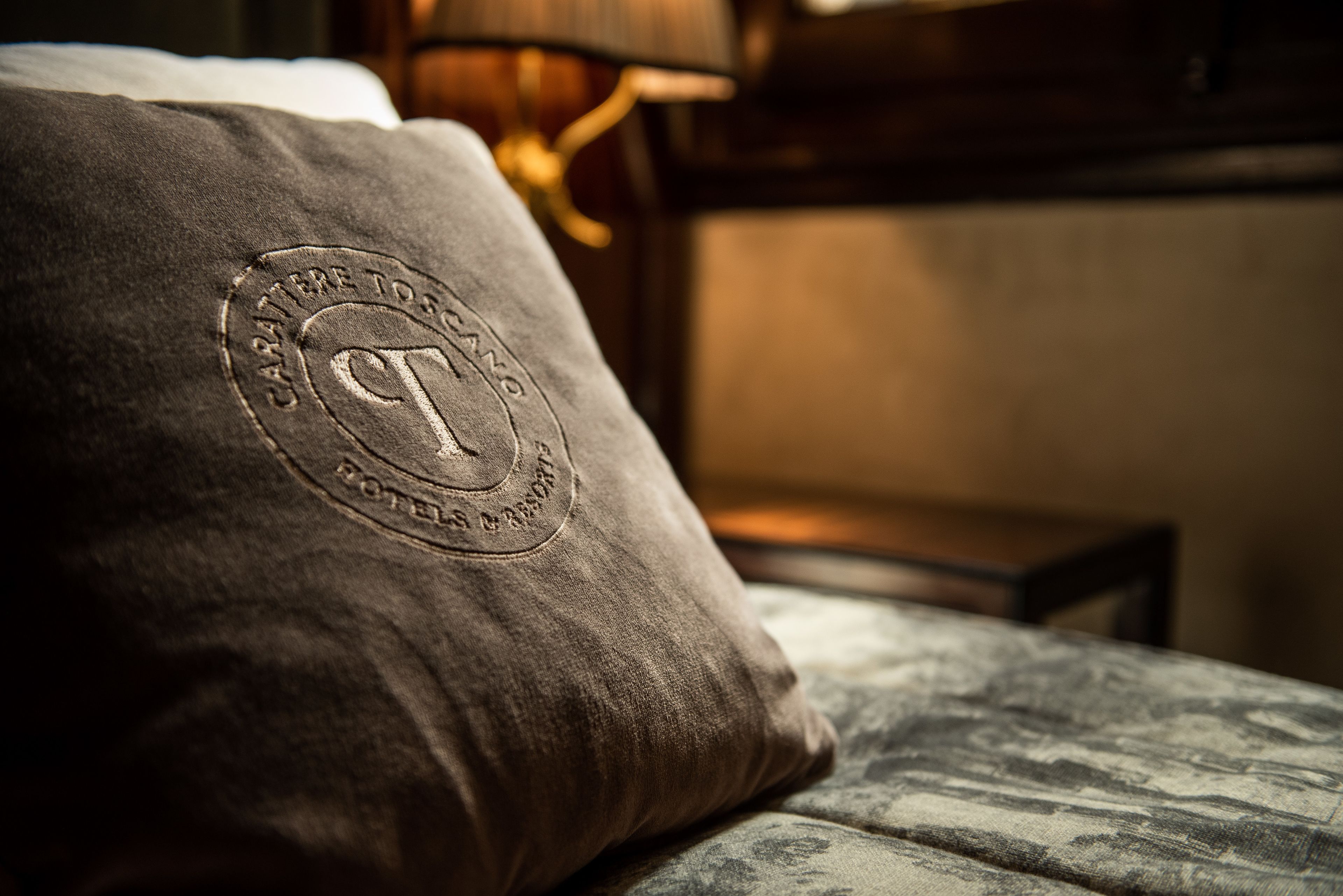 A pillow with a circular embossed logo on a bed.