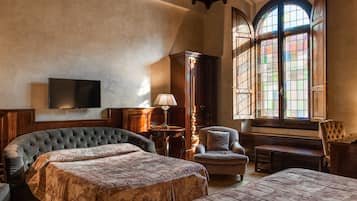 A room with a large bed, a smaller bed, a chair, a desk, and a television on the wall.