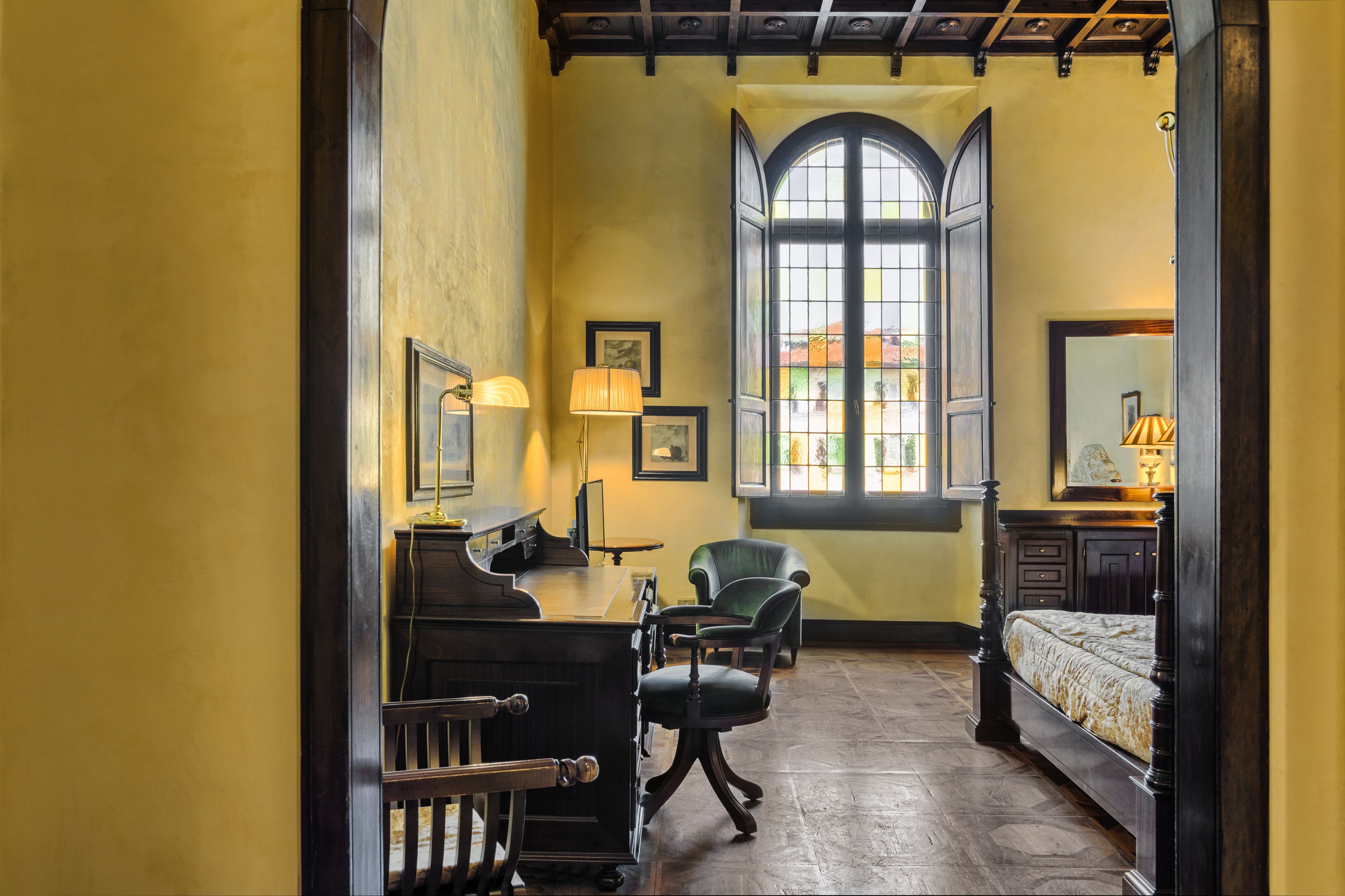 Una habitación con un piano, un escritorio, una silla, una cama y un amplio ventanal de arco.