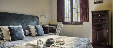 A bedroom with a large bed, a nightstand, a desk, a chair, and a wardrobe.