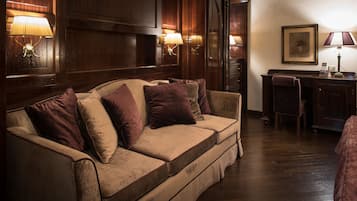 A cozy room with a wooden panel wall, a beige sofa with purple cushions, a desk with a chair, and wall-mounted lamps.