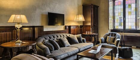 Una sala de estar acogedora con un sofá grande, dos sillones, una mesa de centro y un televisor montado en la pared. Se ve una ventana con vistas al exterior.