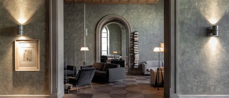 A modern interior with a geometric patterned floor, a central seating area with sofas, and a bookshelf.