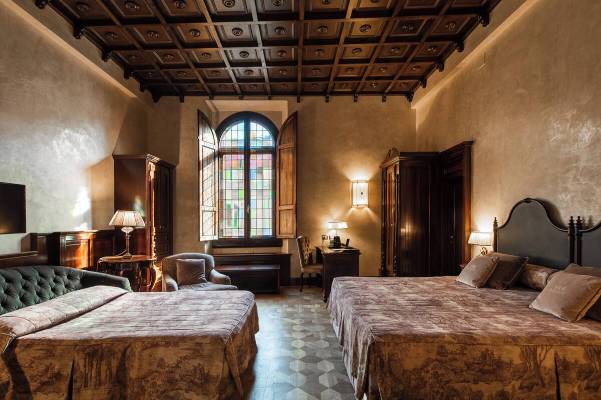 Ein Zimmer mit zwei Betten, einem großen Rundbogenfenster, Holzboden und einem Fernseher an der linken Wand.