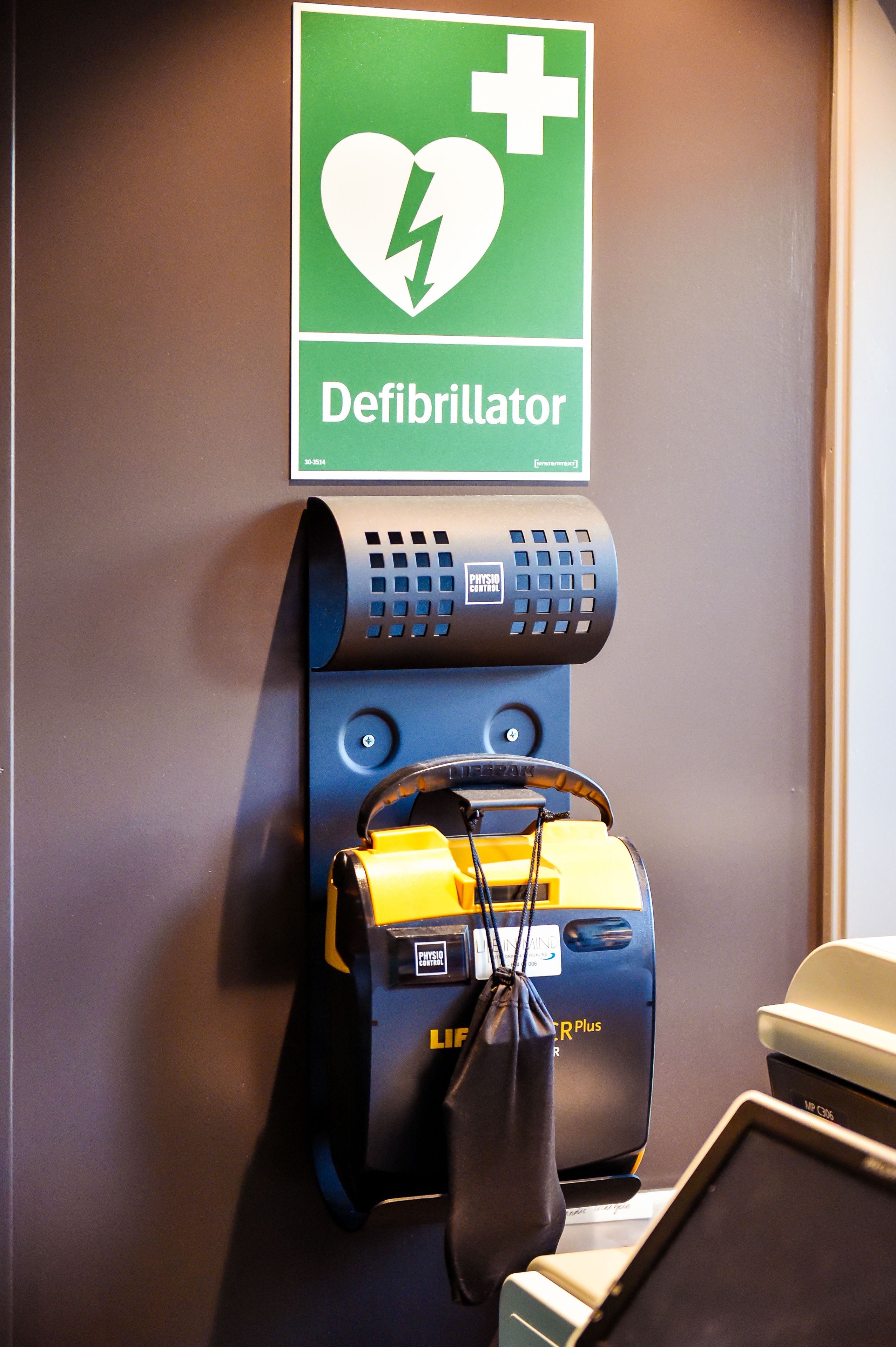 A defibrillator mounted on a wall with a heart and lightning bolt symbol, a portable defibrillator, and a charging device.