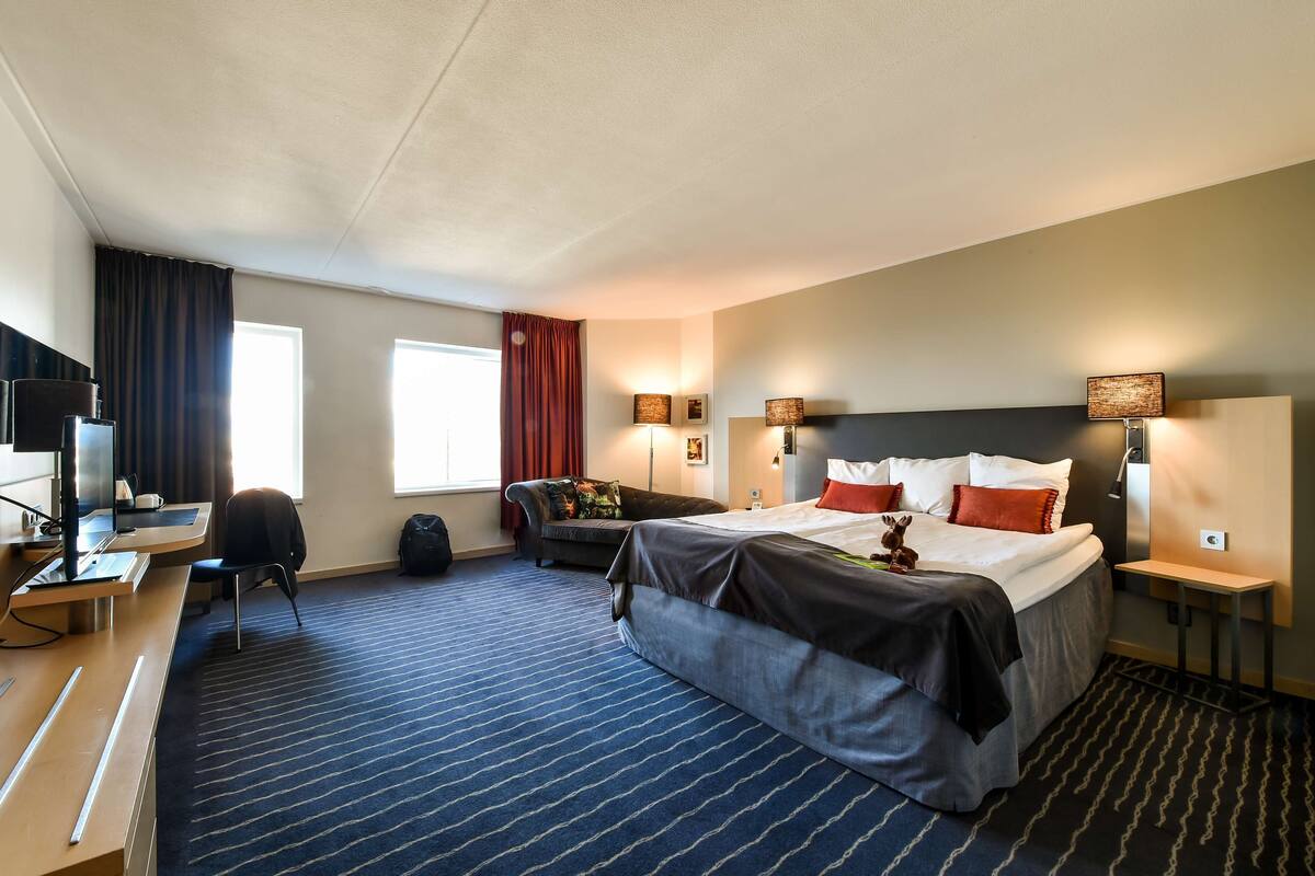 A hotel room with a bed, desk, chair, and a TV.