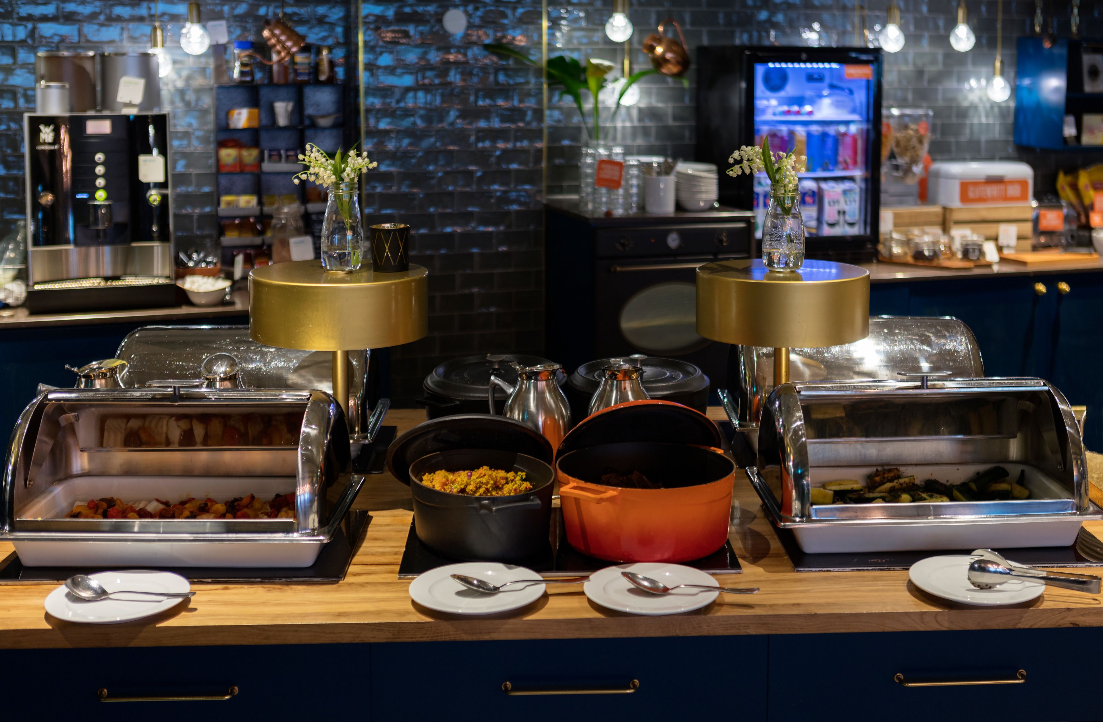 A buffet setup with various food containers, a coffee machine, and decorative vases.