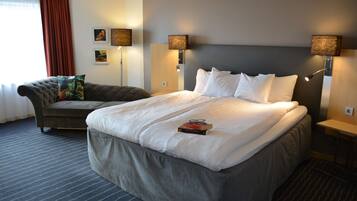 Ett hotellrum med en stor säng, en soffa, två vägglampor och ett fönster med gardiner.