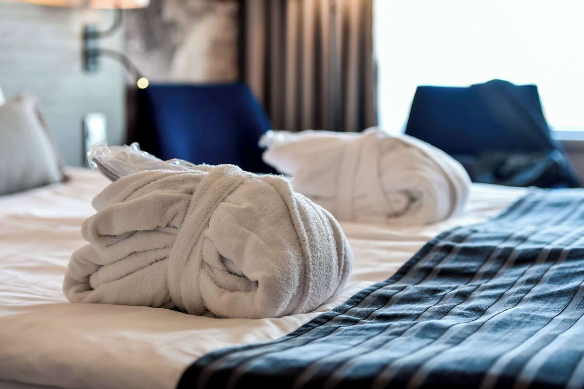 A neatly made bed with a rolled white towel and a blue striped blanket.