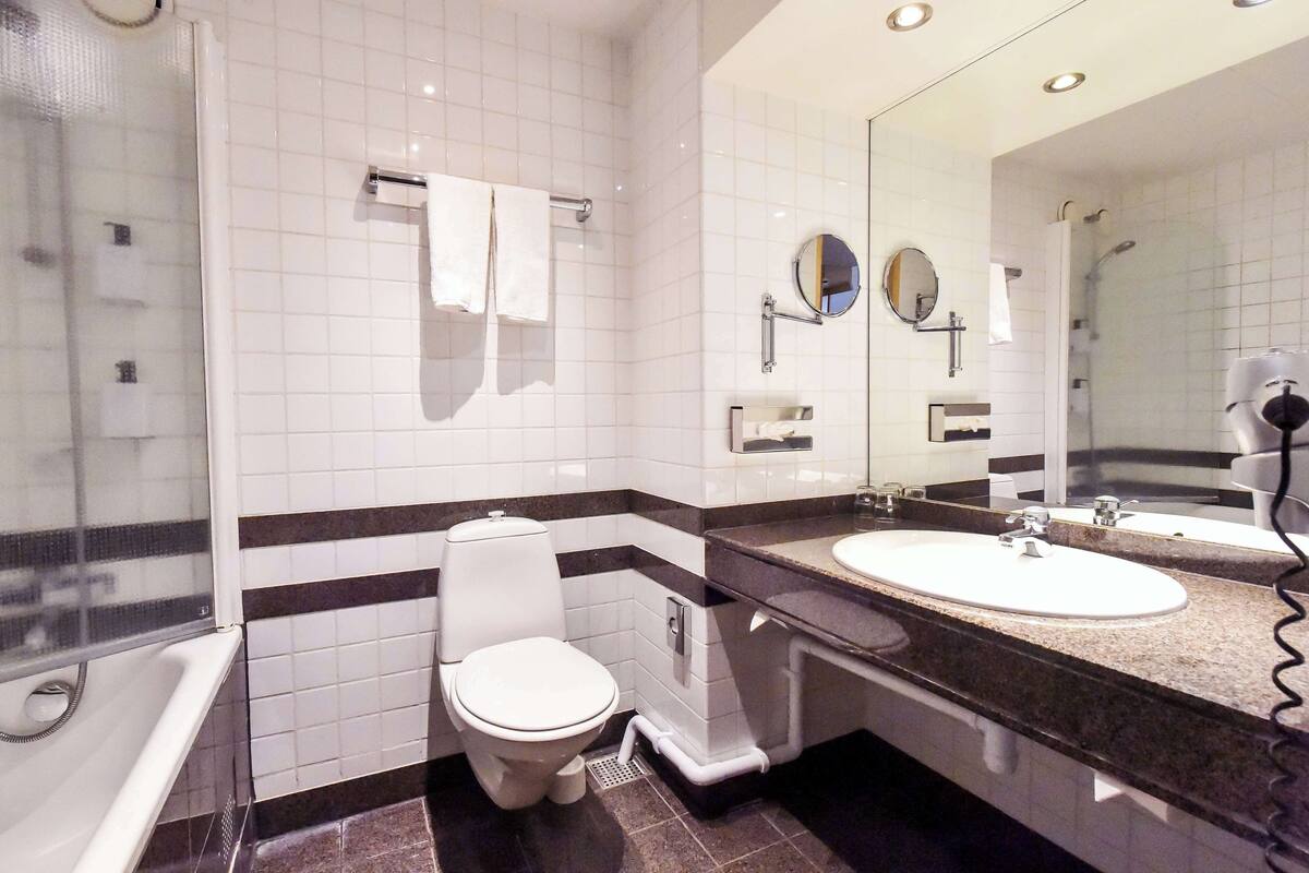 A modern bathroom with white tiles, a toilet, a sink, a mirror, and a shower.