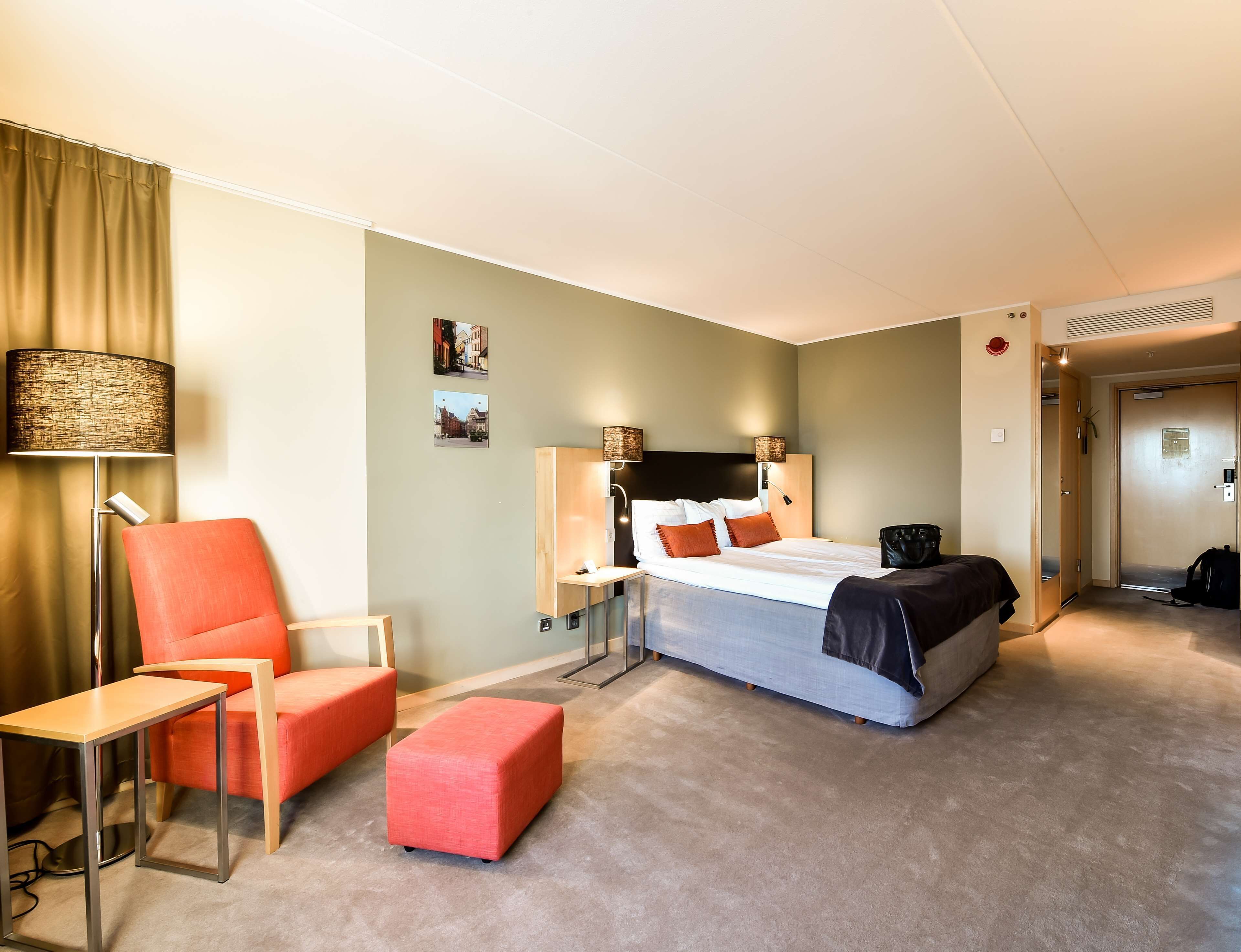 A hotel room with a bed, a desk, a chair, and a small ottoman.