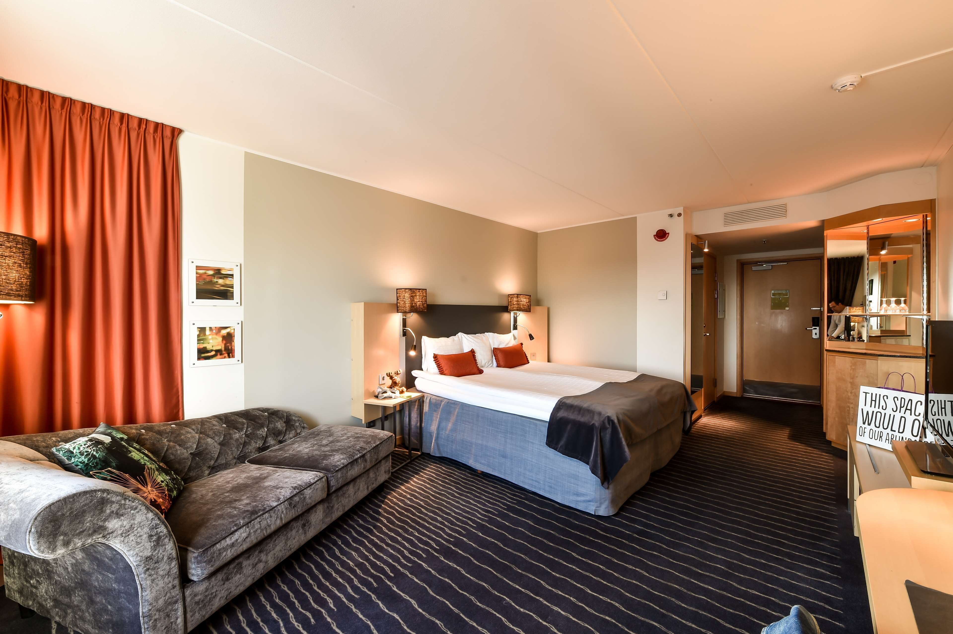 A hotel room with a bed, a sofa, a desk, and a mirror.