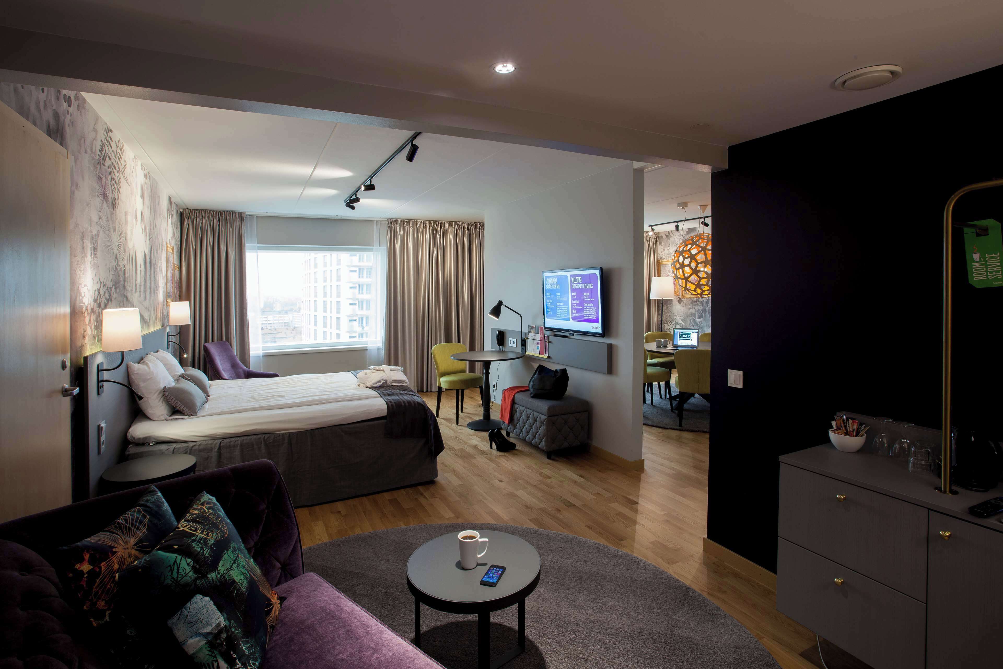 Une chambre d’hôtel moderne équipée d’un lit, d’un canapé, d’une table basse et d’un espace bureau avec un ordinateur et une télévision.