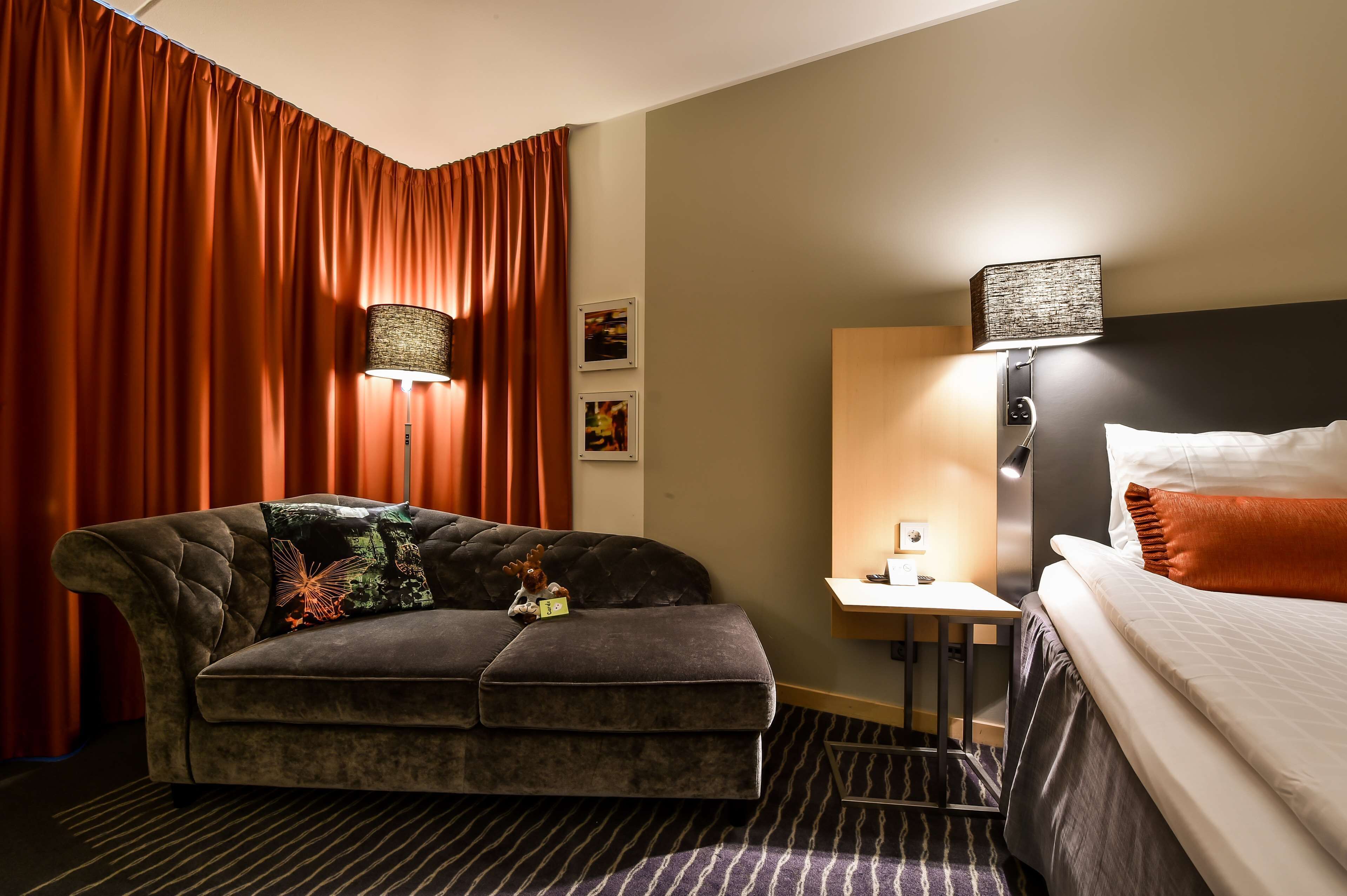 Una camera d'albergo con un divano, un letto, un comodino e una lampada.