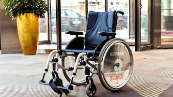 A wheelchair in a public space with a large potted plant and a patterned floor.