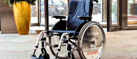 A wheelchair in a public space with a large potted plant and a patterned floor.