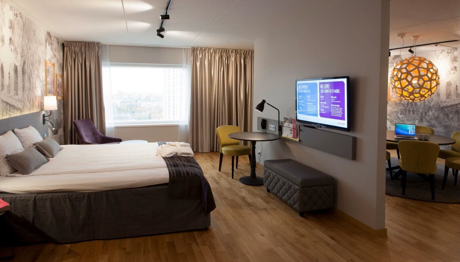 Ett hotellrum med en stor säng, ett skrivbord med en bärbar dator, en tv och en sittgrupp med stolar.