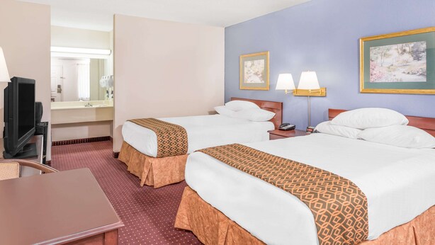 A hotel room with two beds, a desk, a TV, a mirror, and artwork on the walls.