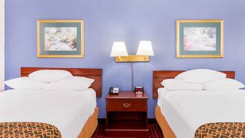 A hotel room with two beds, a nightstand with a lamp, and two framed pictures on the wall.