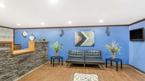 A reception area with a stone wall, a black leather sofa, two side tables with vases, and a large abstract painting on the wall.