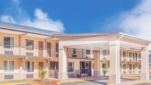 A multi-story hotel with a covered entrance, balconies, and a parking area.
