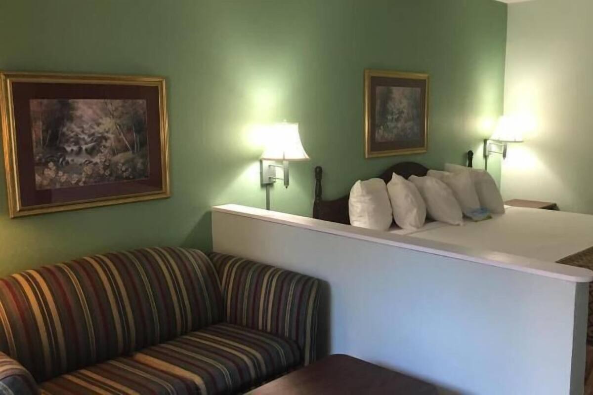 A hotel room with a bed, a striped sofa, two wall-mounted lamps, and two framed pictures.