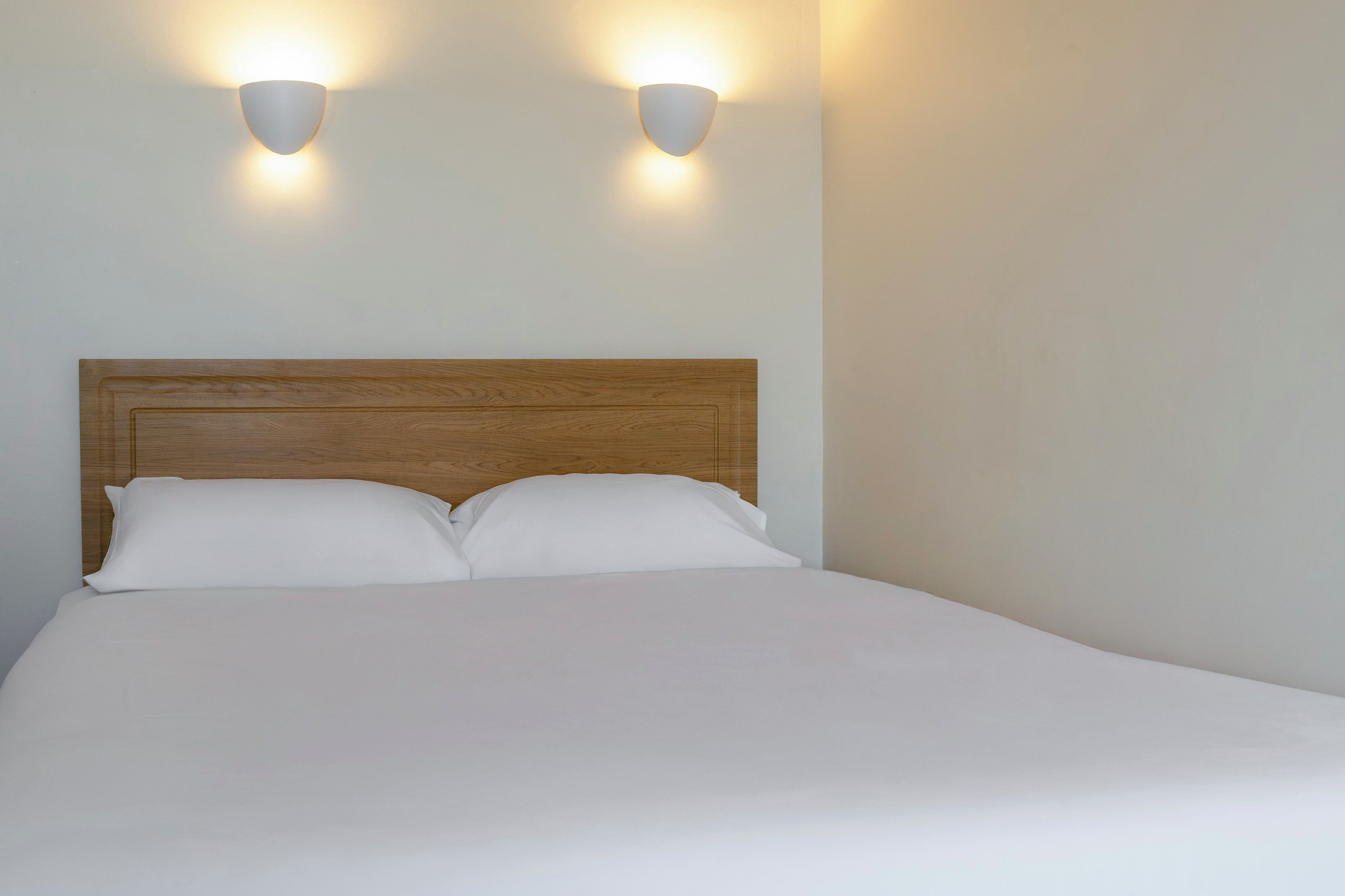 Een opgemaakt bed met een houten hoofdbord en twee wandlampen.