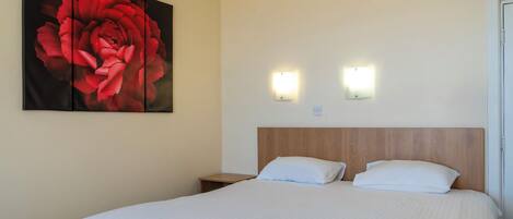 Ein Hotelzimmer mit einem großen Bett, zwei Nachttischen, einem Holz-Kopfteil und einer Wandleuchte.