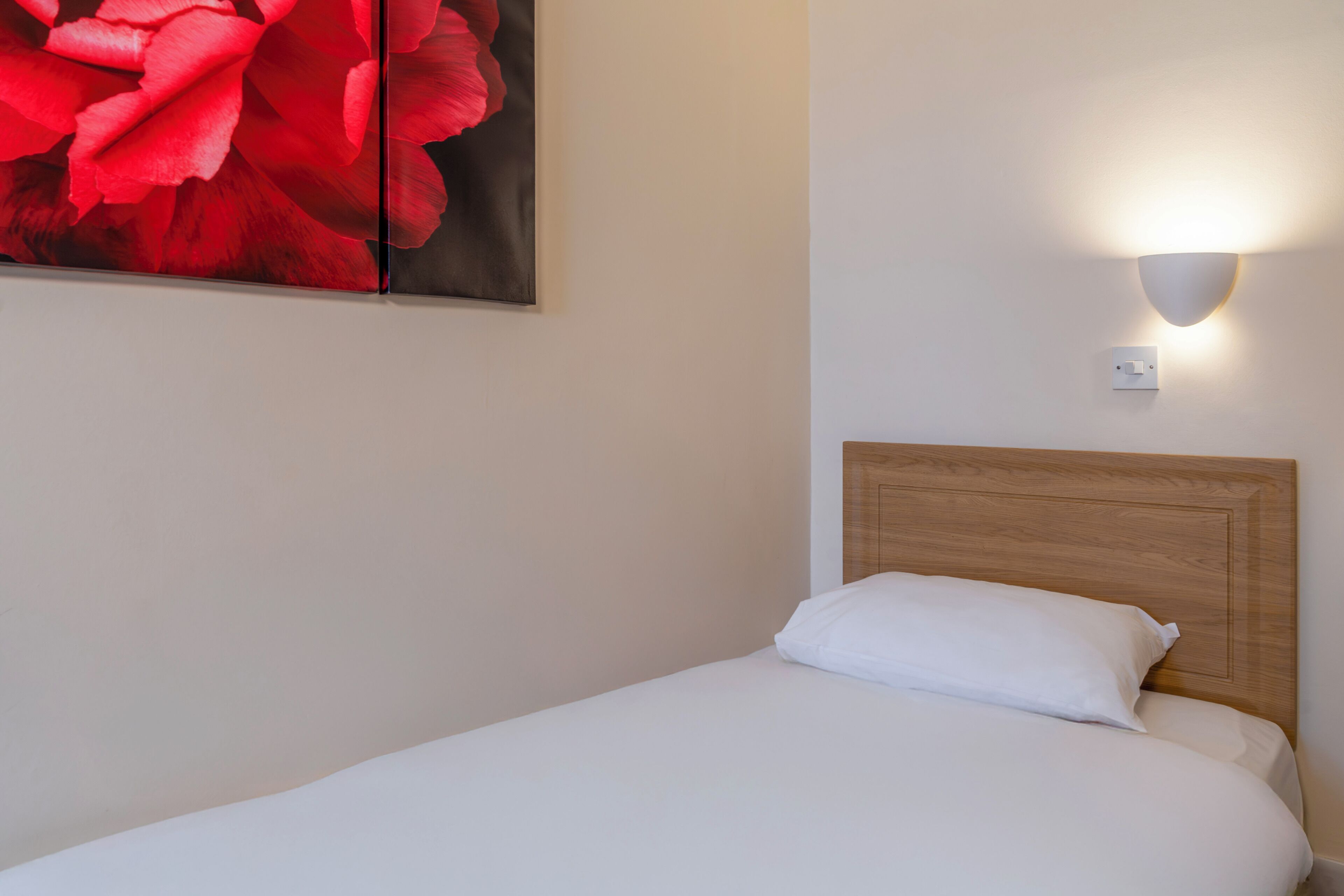 A neatly made bed with white bedding, a wooden headboard, and a wall-mounted light fixture.