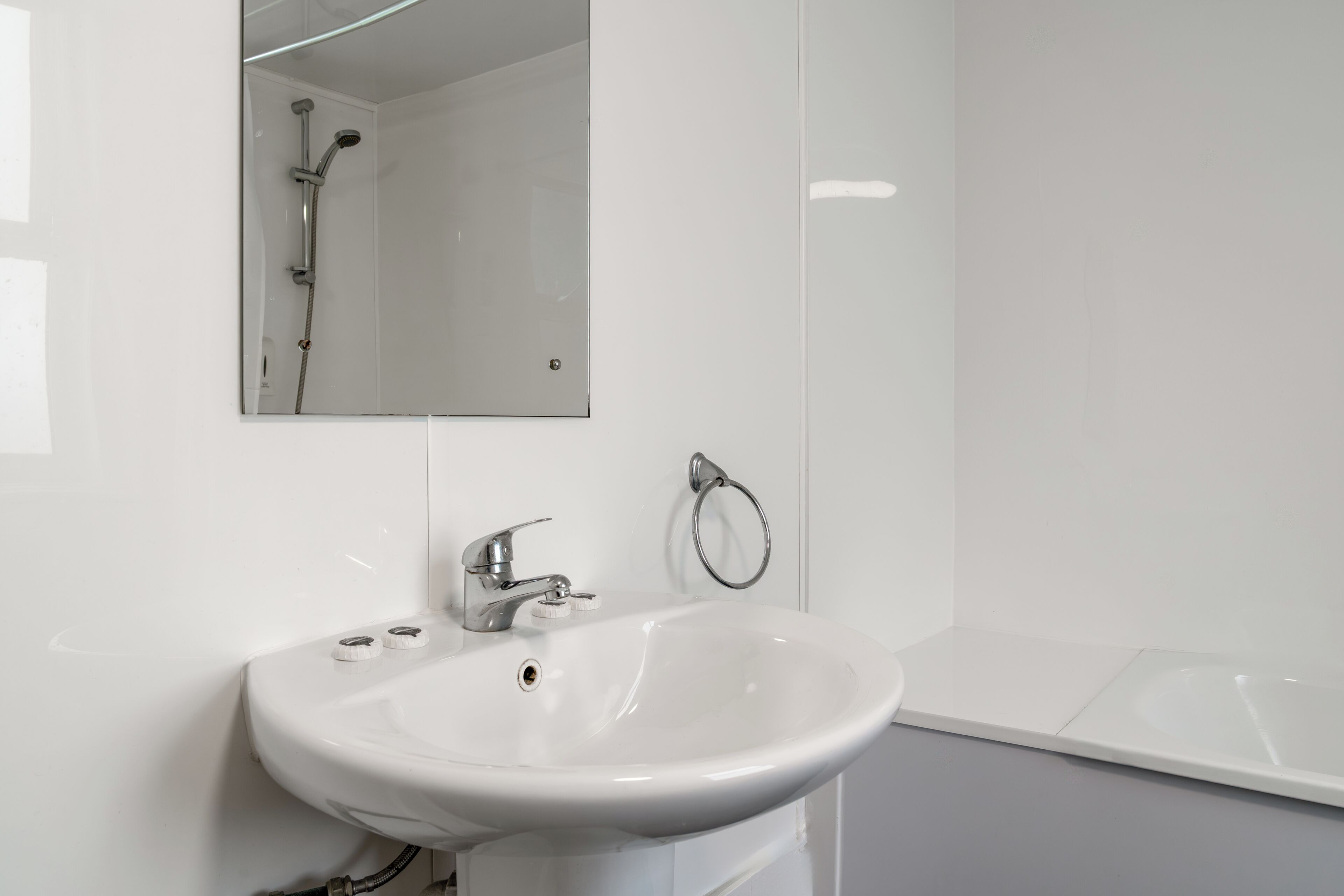A bathroom with a white sink, a mirror, a towel ring, and a shower.