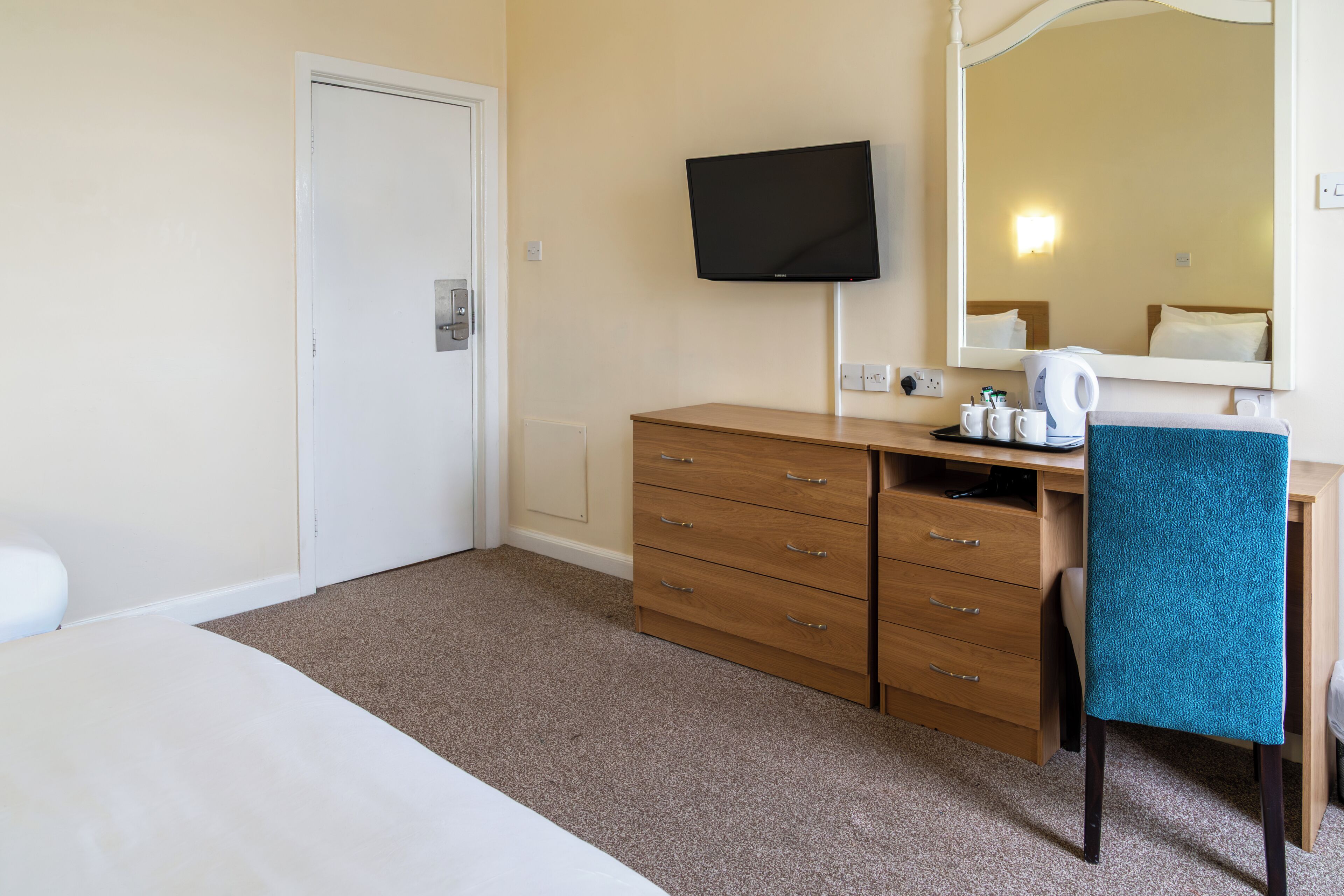 Een hotelkamer met een bed, een houten dressoir, een bureau met stoel, een aan de muur bevestigde televisie en een grote spiegel.