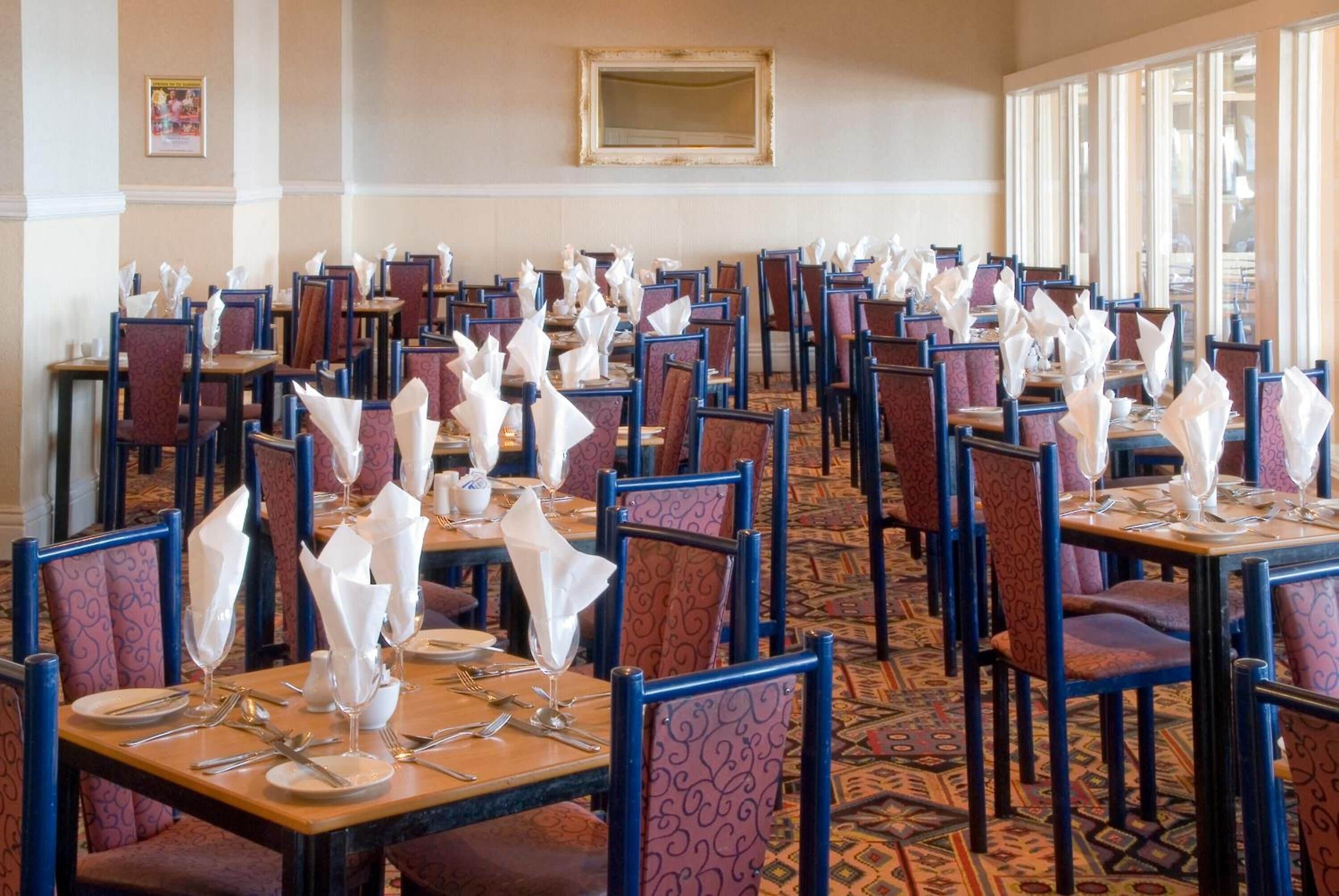 A dining area with multiple tables set with white napkins, silverware, and wine glasses.